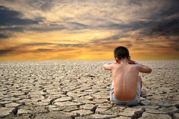 Fototapeta na wymiar Sad a boy sitting on dry ground .concept drought and hope