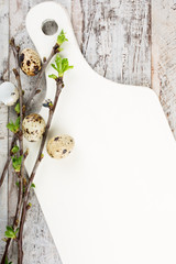 Quail eggs, green branches and white cutting board on old wooden background. Easter background with copy space for text. 