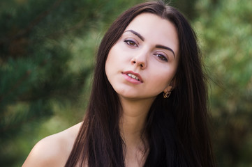 Naklejka premium Graceful charming brunette model posing in black dress in coniferous park