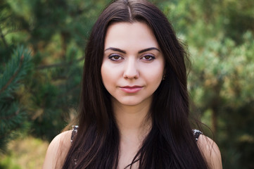 Naklejka premium Graceful charming brunette model posing in black dress in coniferous park