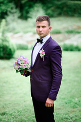 handsome and young groom in blue suit standing outdoors