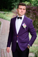 handsome and young groom in blue suit standing outdoors