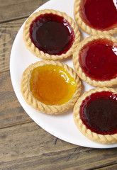 A plate full of assorted fruit jam tarts on a rustic wooden table top background