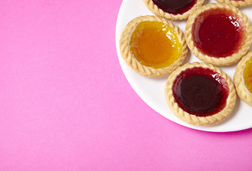 A plate full of assorted fruit jam tarts on a bright pink background with blank space at side