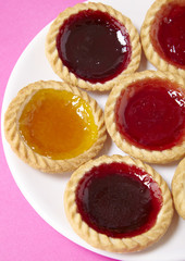 A plate full of assorted fruit jam tarts on a bright pink background