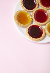 A plate full of assorted fruit jam tarts on a pastel pink background with blank space below