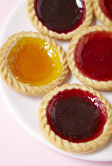 A plate full of assorted fruit jam tarts on a pastel pink background