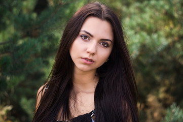 Obraz premium Graceful charming brunette model posing in black dress in coniferous park