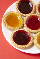 A plate full of assorted fruit jam tarts on a bright red background