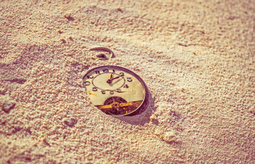 Sands of time. Antique rotten pocket watch buried in the sand, o