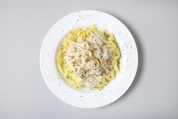 Aerial view of a dinner dish full of tagliatelle spaghetti with a creamy mushroom pasta sauce, on a pastel grey background