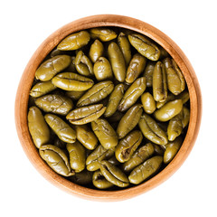 Dried green olive halves in a wooden bowl. Half table olives, dried ripe fruits of Olea europaea. Isolated macro food photo close up from above on white background.