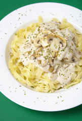 A dinner dish full of tagliatelle spaghetti with a creamy mushroom pasta sauce, on a green background