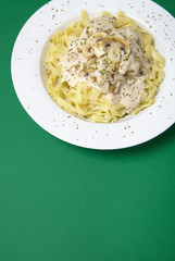 A dinner dish full of tagliatelle spaghetti with a creamy mushroom pasta sauce, on a green background with blank space below