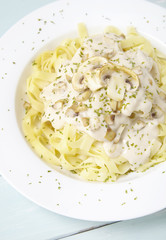 A dinner dish full of tagliatelle spaghetti with a creamy mushroom pasta sauce, on a blue wooden table background