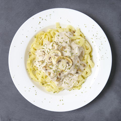 Aerial view of a dinner dish full of tagliatelle spaghetti with a creamy mushroom pasta sauce, on a rustic slate background
