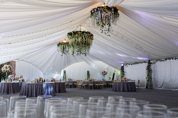Look over empty glassware at white tent prepared for wedding din