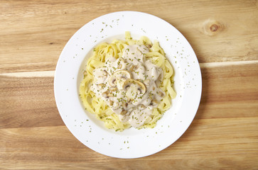 Aerial view of a dinner dish full of tagliatelle spaghetti with a creamy mushroom pasta sauce, on a wooden counter top background