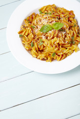 A dinner dish full of tomato and basil fusilli pasta on a painted wooden dining table background with empty space below