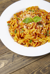 A dinner dish full of tomato and basil fusilli pasta on a rustic wooden dining table background