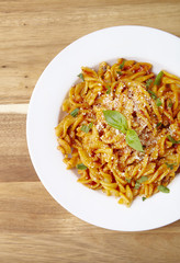 Overhead view of a dinner dish full of tomato and basil fusilli pasta on a wooden kitchen counter background