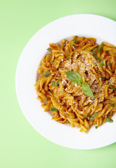 Overhead view of a dinner dish full of tomato and basil fusilli pasta on a pastel green background