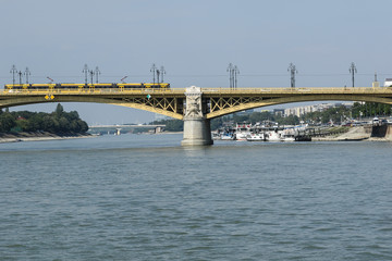 Yellow tram on the yellow Margaret bridge across the Danube river with cruise ships dock in Budapest