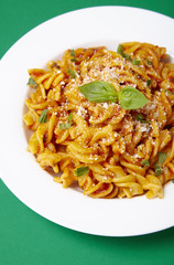 A dinner dish full of tomato and basil fusilli pasta on a green background