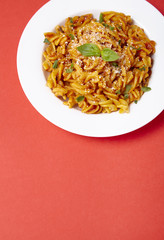 A dinner dish full of tomato and basil fusilli pasta on a bright red background with empty space below