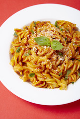 A dinner dish full of tomato and basil fusilli pasta on a bright red background