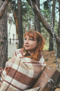 Beautiful red haired young woman with blanket on a bench at the autumn park. Coloring and processing photo