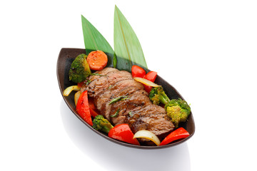 Roasted veal with vegetables on a black plate isolated on white background