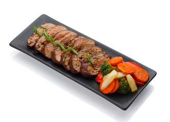 Roasted veal with vegetables on a black plate isolated on white background