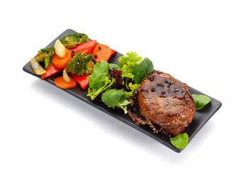 Veal steake with vegetables on a black plate isolated on white background