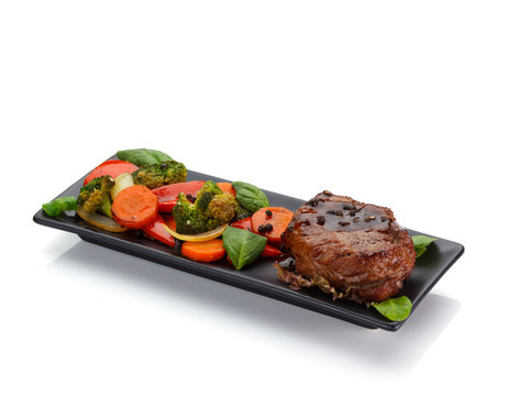 Veal steake with vegetables on a black plate isolated on white background