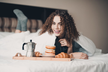 Happy beautiful woman with afro curls eating breakfast in bed. Looking at camera. Good morning.