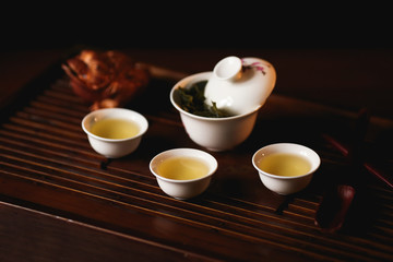 Chinese tea ceremony. Porcelain gaiwan, three cups of Chinese tea and golden frog on tea desk. Soft selective focus.