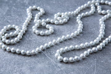 a strand of pearls and perfume on a stone background