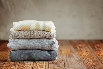 Stack of knitted winter clothes on wooden background, sweaters, space for text