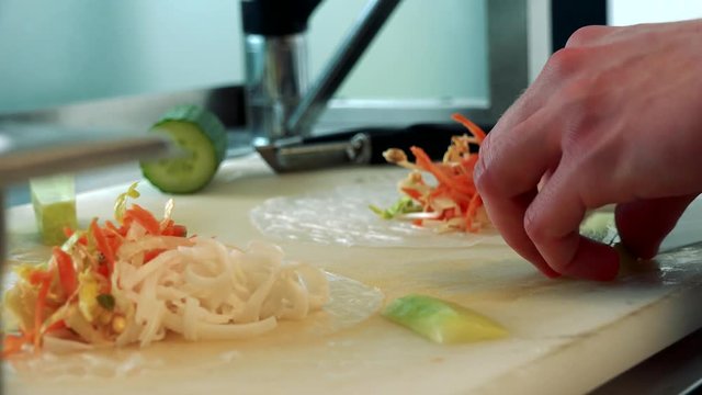 Cook prepares a spring rolls and cuts a cucumber on slices
