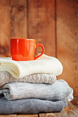 Sweaters Closeup, Stack of knitted winter clothes with red mug on wooden background.