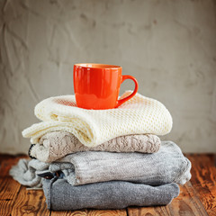 Sweaters Closeup, Stack of knitted winter clothes with red mug on wooden background.