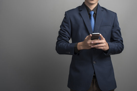 Close up of businessman in blue suit using smartphone on gray ba - Powered by Adobe