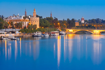 Obraz na płótnie Canvas Dodecagonal military watchtower Golden Tower or Torre del Oro and bridge Puente San Telmo during evening blue hour, Seville, Andalusia, Spain