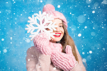 Winter portrait of a beautiful woman in knitted pink scurf, gloves and hat with snow flake on the blue background
