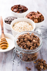 Homemade chocolate granola ingredients, nuts, oats, honey on white wooden background. Healthy brakfast concept.