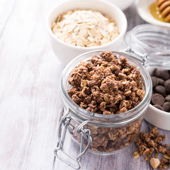 Homemade chocolate granola ingredients, nuts, oats, honey on white wooden background. Healthy brakfast concept with copy space.