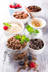 Homemade chocolate granola ingredients, nuts, oats, honey and berries on white wooden background. Healthy brakfast concept.