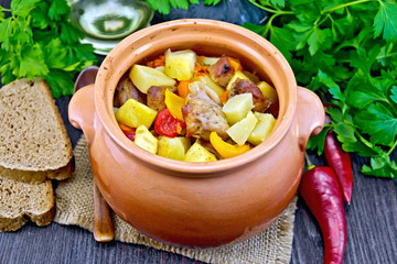 Roast meat and potatoes in clay pot on dark board