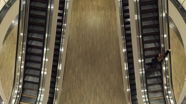 The girl up the escalator, she is shopping in the mall
